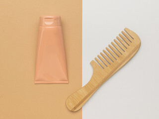 A wooden comb with a handle and a hair care product on a white and beige background.