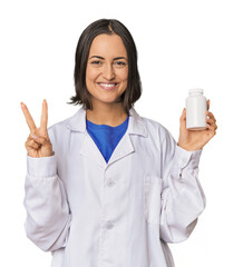 Young Caucasian female pharmacist with pills showing number two with fingers.