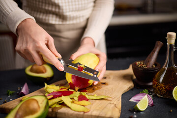 Woman peeling mango on a wooden cutting board at domestic kitchen