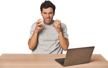 Hispanic young man working on laptop upset screaming with tense hands.