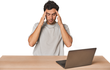 Hispanic young man working on laptop touching temples and having headache.
