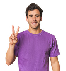 Young Hispanic man in studio joyful and carefree showing a peace symbol with fingers.