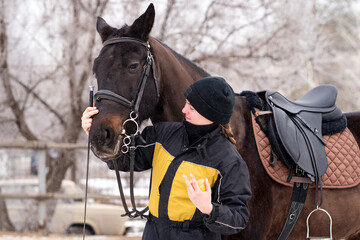 Person feeding apple to horse in snowy setting.