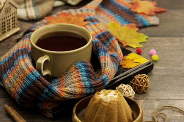 Autumn mood in the form of a cup of tea and a warm scarf. Maple leaves are scattered on a wooden...