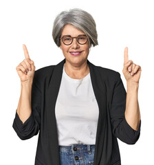 Caucasian mid-age female in business suit indicates with both fore fingers up showing a blank space.