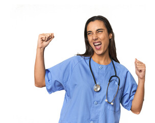 Hispanic nurse in uniform with stethoscope raising fist after a victory, winner concept.