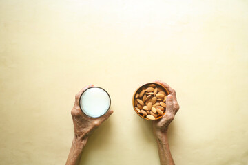 top view of senior women hand holding a bowl of almond nut and a glass of milj 
