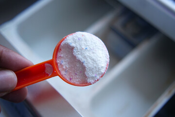 Washing powder in plastic spoon on black background top view.