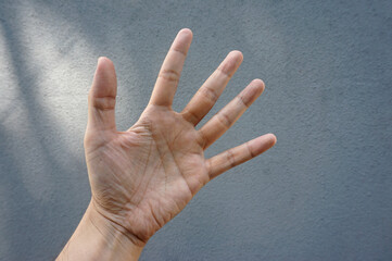 Closeup of hand showing five fingers isolated on grey background outdoor