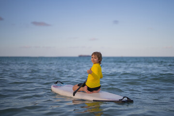 Obraz premium Kid Paddle boarder. Child boy paddling on paddleboard. Healthy summer lifestyle. Summer Water sport. SUP surfing tour in adventure summer beach vacation. Kid Boy swimming with paddle board.