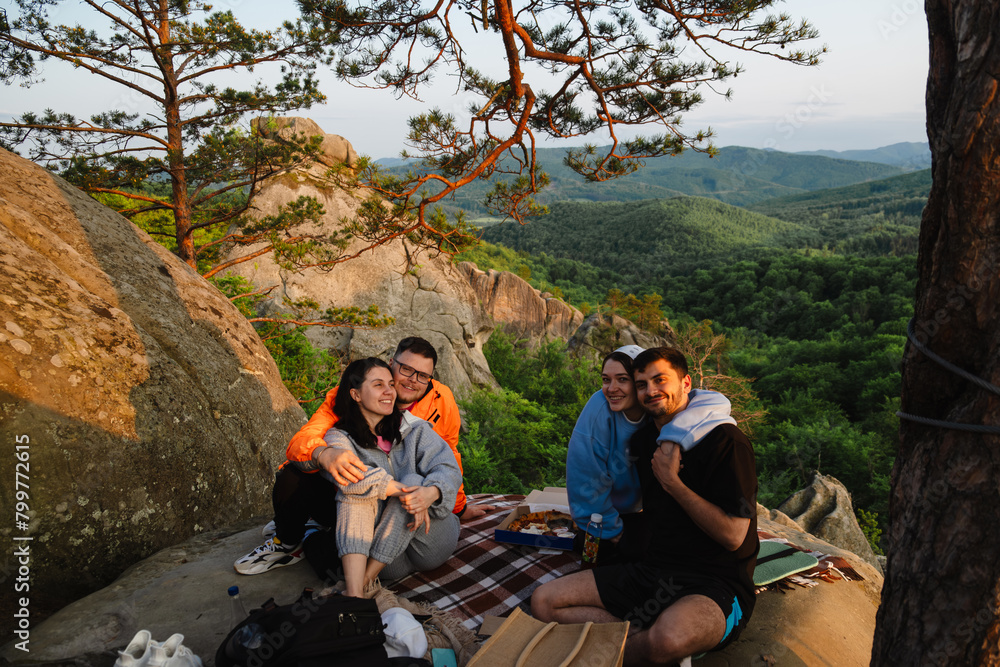 Poster happy friends eating pizza at the cliff with beautiful mountain view