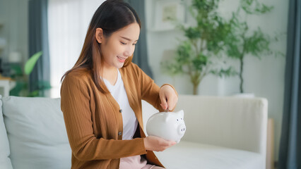 Young Asian woman putting coin in piggy bank. Save money and financial investment