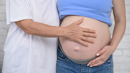 An elderly woman touches the belly of her pregnant daughter. Close-up.