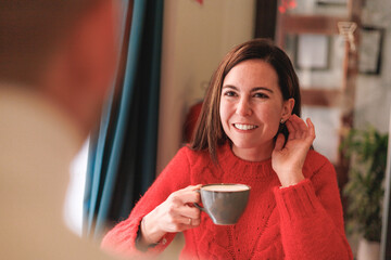 Young woman drinking coffee and listening happily to her male friend. Two friends talking in a cafe