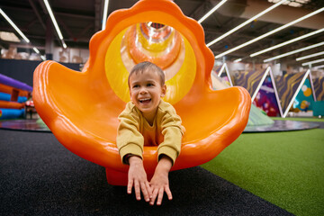 Cute little boy child riding on slide at indoor playground