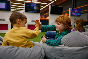 Happy boys siblings wining competition while playing video game in kids center
