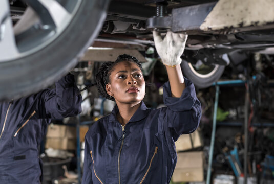 Black auto mechanic woman fixing car in auto repair  garage - Powered by Adobe