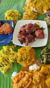 Traditional Indian boiled rice served on green banana leaf with various spices, curry, vegetables and meat. Top view, vertical video format.