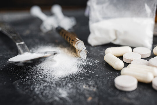 Narcotic substances in spoon, dope powder in transparent plastic bag, syringes with drugs dose, white pills on dark textured background. Concept of addiction and bad habits