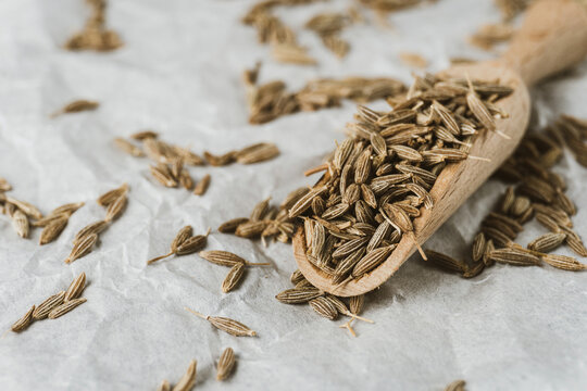 Dried caraway cumin seeds in wooden spoon and pile of zira nearby on white crumpled paper. Closeup