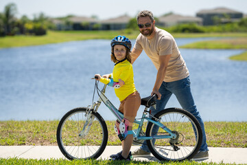 Fototapeta premium Father and son in a helmet riding bike. Little cute adorable caucasian boy in safety helmet riding bike with father. Family outdoors summer activities. Fathers day. Childhood and fatherhood.