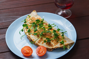 Tasty pork quesadillas with tomato and pea stalks in blue plate on wooden table. Mexican tacos