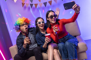 Happy asian diverse group friends taking selfie with neon light on a party using smartphone. Home party friends having fun enjoying time and dancing together. New Year's Eve Party concept.