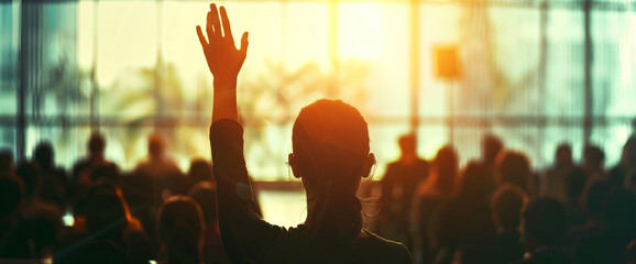 The hand of one person was raised in the audience while listening to an interview at a business conference or presentation. During the training class, people were sitting and raising their hands to as