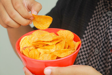 Close up a man's hand holds a bowl of potato snack. Isolated in gray background.