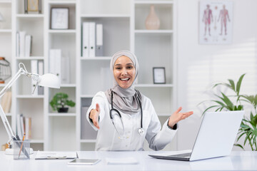 A warm and inviting female doctor wearing a hijab extends her hand in greeting, sitting at her desk...