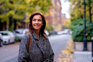 Brunette haired woman wearing tweed coat and walking outdoors in the city street on autumn day - obrazy, fototapety, plakaty