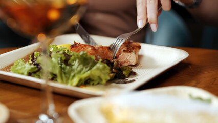 The girl cuts well-cooked, juicy meat on an ecological plate with a knife and fork. Delicious food without harm to the environment.