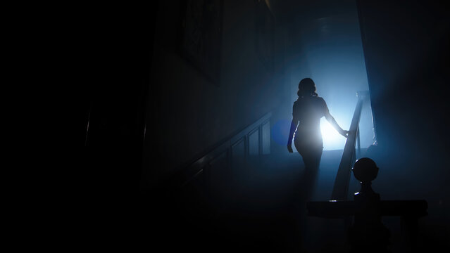 Beauty and form. The silhouette of a beautiful, young woman against a dark background is climbing up the old stairs.