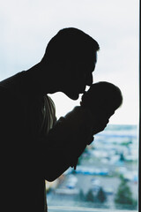 A young loving dad holds his son in his arms against the background of the window.