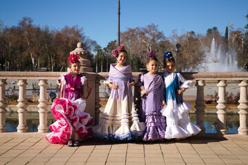 four pretty little girls dancing flamenco dressed in typical gypsy costume pose in a famous square...
