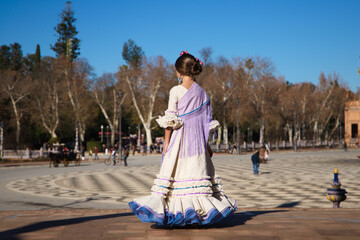 a little girl dancing flamenco dressed in a beige dress with ruffles and purple fringes in a famous...