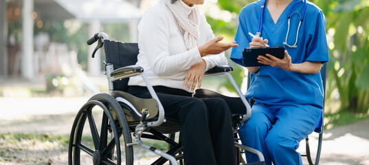 Elderly asian senior man on wheelchair with Asian careful caregiver. Nursing home hospital garden...