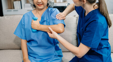 Physiotherapist helping elderly woman patient stretching arm during exercise correct with dumbbell...