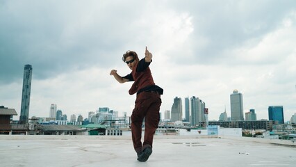 Motion shot of B-boy dance performance by professional street dancer at rooftop with sky scrapper,...