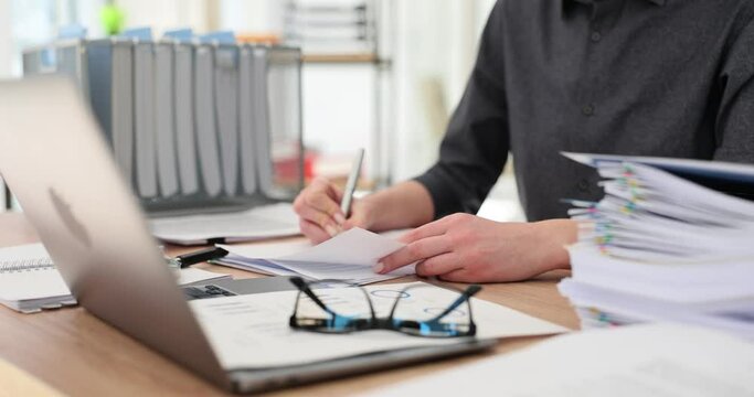 Woman manager fills out work papers sitting at table at workplace in office premise. Concept of working with documents and checking report slow motion