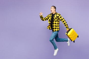 Young traveler man he wear yellow casual clothes hold bag run fast isolated on plain purple background studio. Tourist travel abroad in free spare time rest getaway. Air flight trip journey concept.