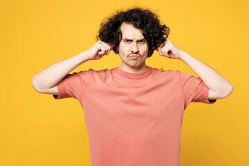 Young sad dissatisfied man he wear pink t-shirt casual clothes cover ears with hands fingers do not want to listen scream isolated on plain yellow orange background studio portrait. Lifestyle concept.