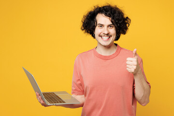 Young smiling smart happy IT man he wearing pink t-shirt casual clothes hold use work on laptop pc...