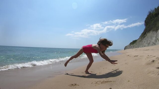 Little girl in pink swimsuit doing a handstand on the beach in summer vacation