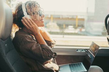 One woman listening music with headphones and computer sitting inside public bus transport enjoying...