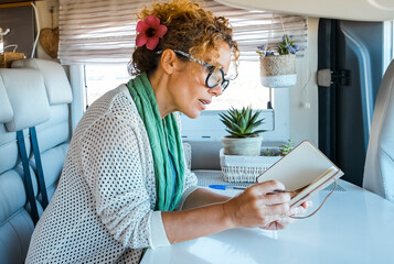 One woman reading a book or writes and plans sitting inside a camper van motorhome. Traveler lady...