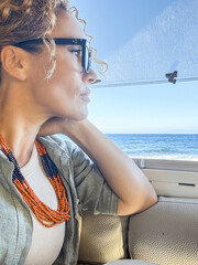 A curly-haired woman with glasses looks out the window of her camper. She vacations at home on...