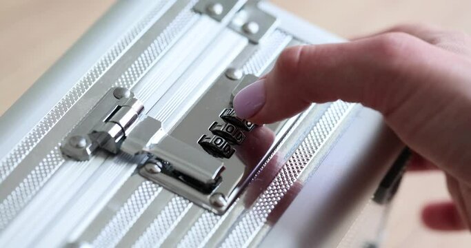 Female hand opens silver briefcase using combination lock. Young woman with neat manicure unlocks metal case on wooden table in office