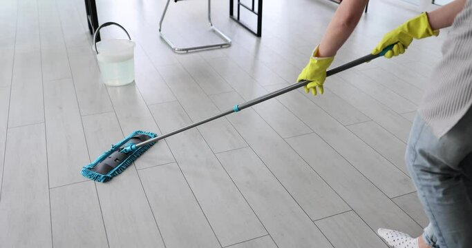 Female in rubber gloves cleans floor with wet mop in renovated apartment. Cleaning service employee works in light room after repair. Sanitary care