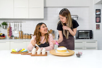 Two women enjoy in a fun cooking or baking activity in a modern kitchen with colorful baking tools or decoration.